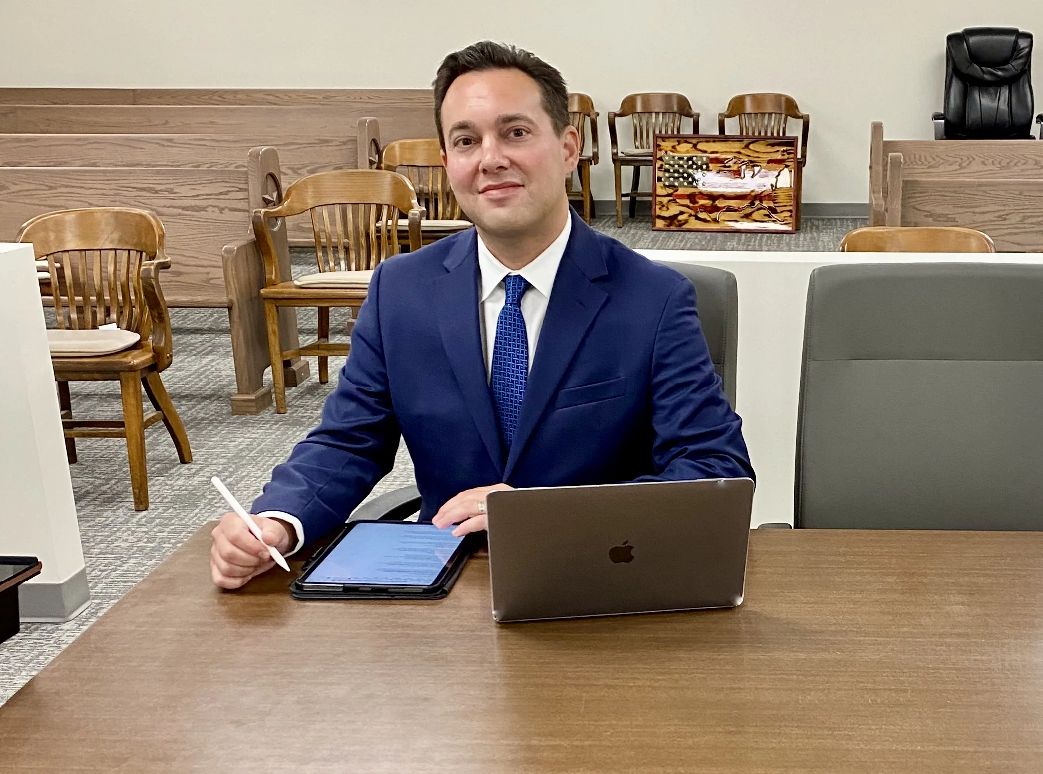 David Smith sitting at counsel table with iPad and MacBook Pro, utilizing AI in his law practice, saving 20+ hours per week.