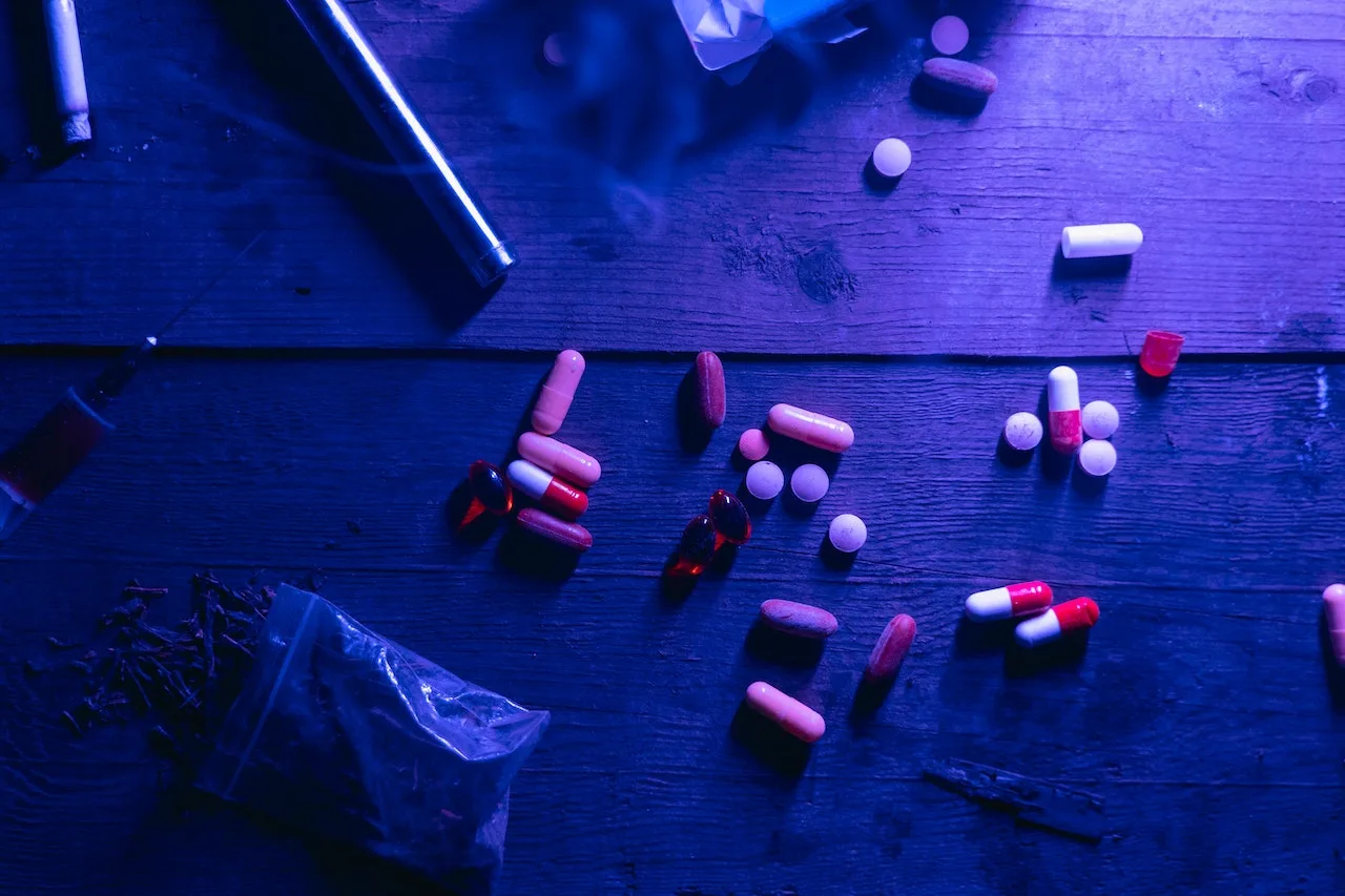 pexels-mart-production-7230391 Assorted pills and a syringe on a dark wooden surface, illustrating drug possession and related criminal charges in the context of criminal defense law.