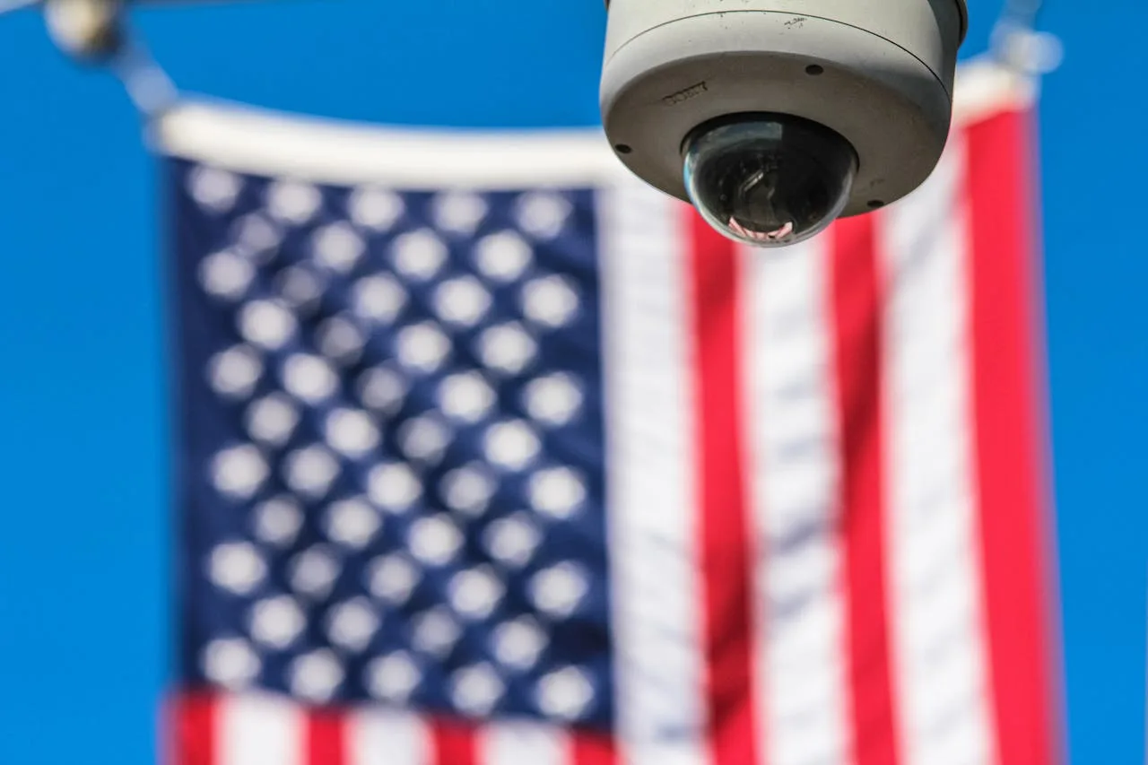 Surveillance camera in focus with American flag in background, symbolizing security and privacy concerns related to Flock cameras in Houston.